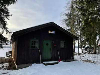 a small cabin with a green door in the snow at Hagali by Norgesbooking - cabin by the lake Næra, close to Sjusjøen in Ringsaker