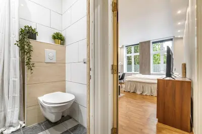 a bathroom with a toilet and a bed in the background at Fløyen Apartments in Bergen
