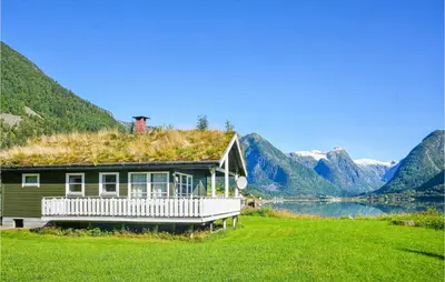 a house with a grass roof with a lake and mountains at Awesome Home In Fjærland in Fjarland