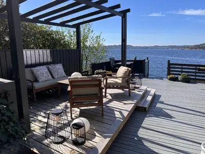 a patio with a table and chairs on a deck next to the water at En Perle ved Masfjorden in Masfjorden