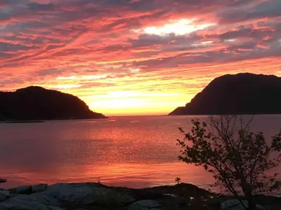 a sunset over a body of water with mountains at Seaside apartment in farmhouse close to nature in Husevåg