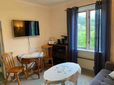 a living room with a table and chairs and a television at Seaside apartment in farmhouse close to nature in Husevåg