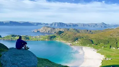 a man sitting on a rock overlooking a beach at Idyllisk overnatting i dome ved sandstrand in Langenes