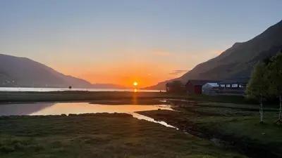a sunset over a river with a barn and mountains at Strandhus i idylliske omgivelser in Batnfjordsøra