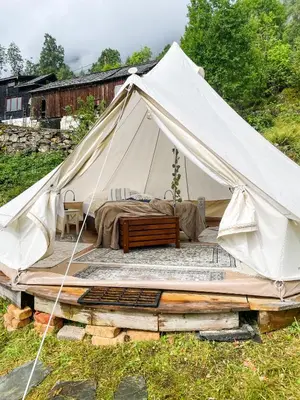 a white tent with a bed on a pile of logs at Glamping Kalhagen in Vangsbygd