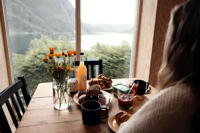 a woman sitting at a wooden table with flowers and wine bottles at Spectacular Fjord getaway - The Forge in Leirgulen