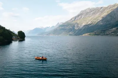 a person in a boat on a lake with mountains at Hardanger Fjord Living in Vossevangen