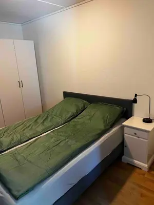 a bed with a green comforter and a side table at Staupslia Apartment in Levanger