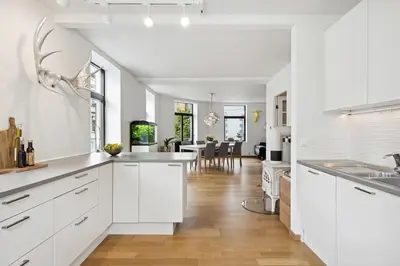 a kitchen with white cabinets and a living room at A Gem in the Heart of Ålesund in Ålesund