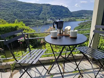 a table and chairs on a balcony with a view of a river at Cozy flat with lake view and 15 min from Bergen in Bergen