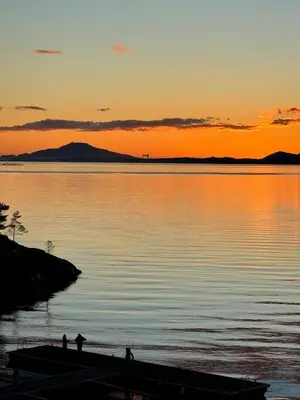 two people standing on a dock in the water at sunset at Gorgeous views and sunsets in Halsnøy, Kvinnherad in Ådnavik