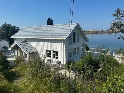a white house sitting next to a body of water at Historic Cabin By The Atlantic Ocean Road in Vevang
