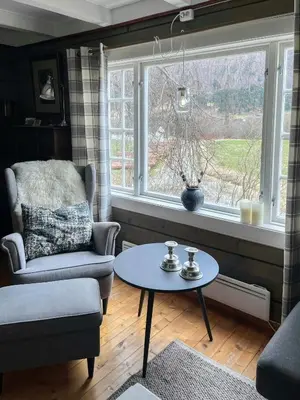 a living room with a chair and a table and a window at Historic Log House At The Foot Of Middagstind in Sæbø