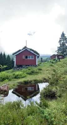 a red barn with a reflection in a field at Historic Log House At The Foot Of Middagstind in Sæbø