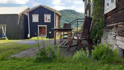 a wooden deck with a chair and a table and a house at Trivelig Stabbur på Lånke Gård