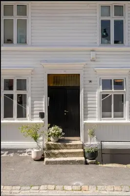 a white house with a black door and two potted plants at Studio apartment centrally located in Bergen in Bergen