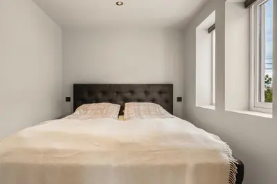 a bed in a white room with two windows at Trolltunga Fjord Stay in Odda