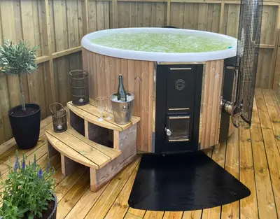 a hot tub in a deck with a table and a bench at Hyggelig Gård Nær Bergen Med Spabad in Hjelmås
