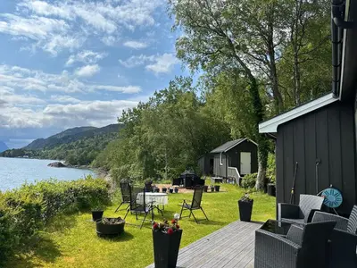 a deck with chairs and a cabin next to the water at Koselig hytte i sjøkanten in Ålesund