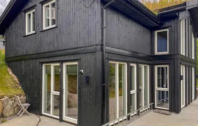 a black house with glass doors and windows at Cozy Home In Hovden I Setesdal - With Jacuzzi in Hovden