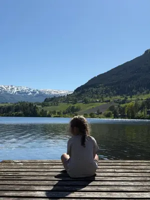 a woman sitting on a dock by a lake at Unique and romantic Lakeside Experience in Vossevangen