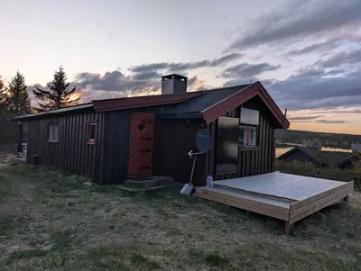 a small cabin with a deck in a field at Nordseter Sjusjøen fiske, jakt, tur og ski in Lillehammer