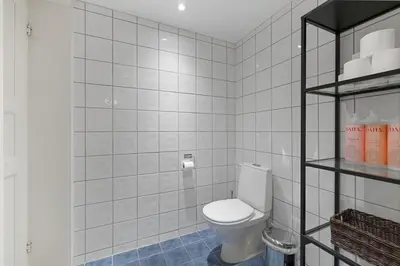 a white tiled bathroom with a toilet and shelves at Central Bergen apt w Balcony in Bergen
