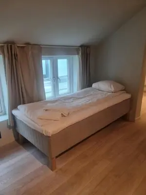 a bed in a room with two windows at Central Apartment for 5 in Trondheim