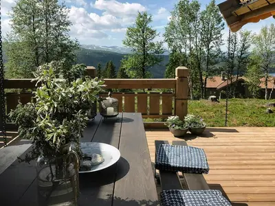 a wooden deck with a table and a view of the mountains at Tømmerhytte Med Utsikt Over Jotunheimen in Gålå