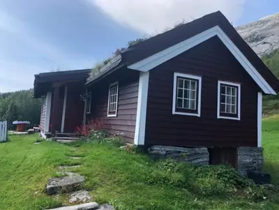 a small black house with a hill in the background at Gamlestova in Viksdalen