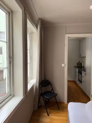 a bedroom with a chair sitting next to a window at Romslig leilighet midt i Bergen sentrum - komfort med kvalitetsenger og dyner in Bergen