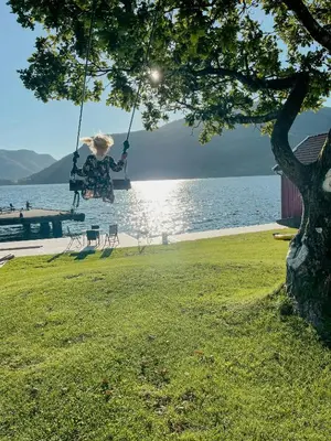 a woman sitting on a swing by the water at Renovated 1918 House By The Sea In Sandeid in Sandeid