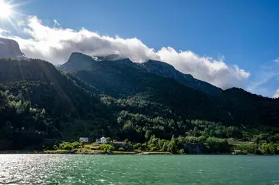 a view of a mountain from a lake with the sun at Hardanger Odda Apartments in Odda