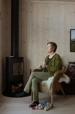 a woman sitting in a chair in front of a fireplace at Authentic Family Cabin Experience At Sjusjøen in Sjusjøen