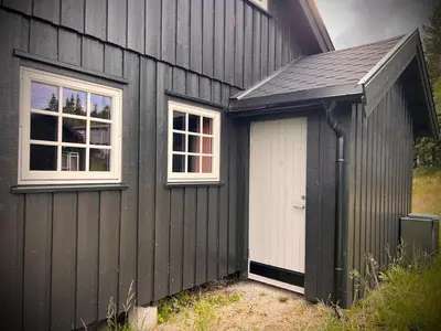 a black building with a white door and two windows at Hytte på Norefjell in Surteberg