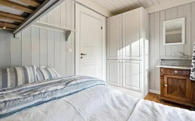 a white bedroom with a bed and a wooden dresser at Cabin with ski in-out in Sør-Fron