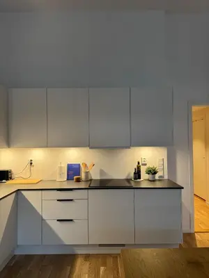 a white kitchen with white cabinets and a wooden floor at Oceanfront Stay, Large Balcony and Rooftop Access in Bergen