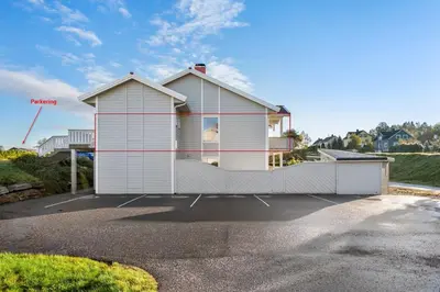 a white house with a fence in a parking lot at Central Langevåg Family Apartment in Sula