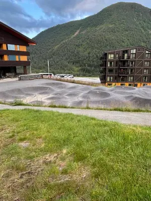 a parking lot in front of a building with a mountain at Apartment vårstølen in Vossevangen