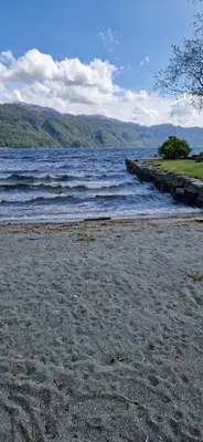 a beach with a large body of water with mountains at Hus ved sjøen, med strand og naust in Sauda