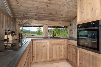 a large kitchen with wooden cabinets and windows at Hedda Robølshøvda - 3 bedroom cabin with a lovely view in Heggenes