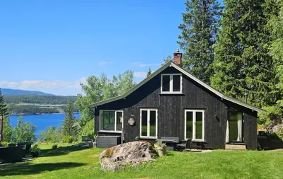 a black house on a lawn with a large rock at WOOD HOUSE GARDEN Lakeview Mjøsa -30 min OSL