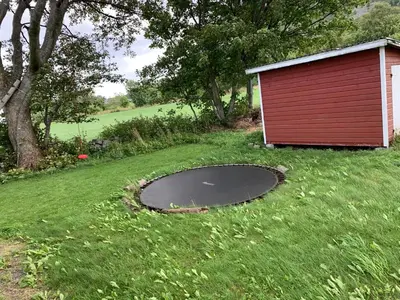 a small red shed with a trampoline in the grass at Flø Feriehus med Badstue in Ulstein