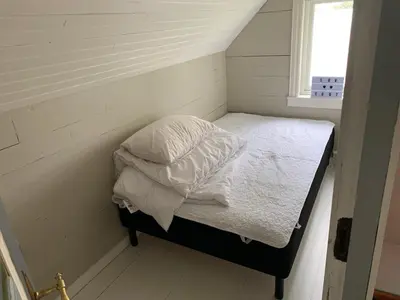 a small bedroom with a bed with white sheets and a window at Flø Feriehus med Badstue in Ulstein