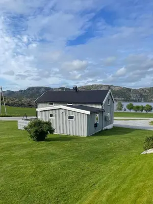 a white barn with a black roof on a grass field at Flott feriehus ved sjøen