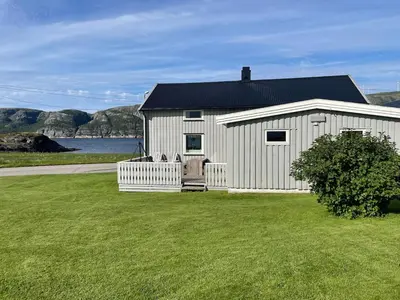 a white building with a fence in a grass field at Flott feriehus ved sjøen