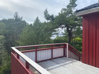 a wooden deck with a red building and trees at Bjørnafjorden