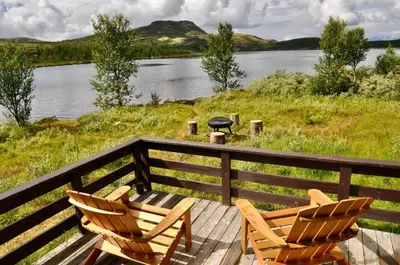 two chairs and a grill on a deck next to a lake at Flaksjøen in Venabygd
