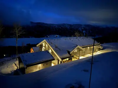 a house covered in snow at night with lights at Log Cabin At The Foot Of Hallingskarvet in Hovet