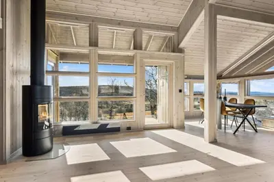 a living room with a fireplace and large windows at Hedda Lenningen - 3 bedroom cabin with view towards Langsua National Park in Etnedal